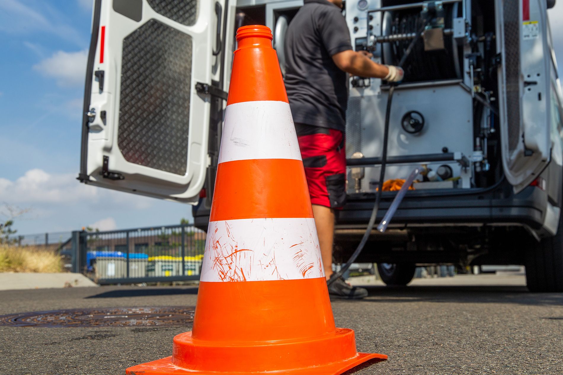 Ein Mann steht hinter einem orange-weißen Verkehrshütchen und holt Arbeitsmaterial aus einem Firmenfahrzeug